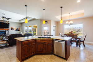 Kitchen with stainless steel dishwasher, a raised ceiling, sink, pendant lighting, and an island with sink