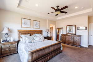 Bedroom with dark colored carpet, a tray ceiling, and ceiling fan