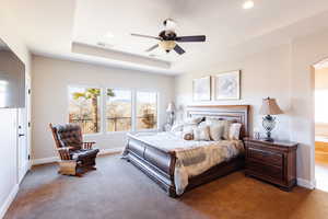 Carpeted bedroom featuring a tray ceiling and ceiling fan