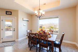 Dining space with a raised ceiling, light tile patterned floors, and an inviting chandelier