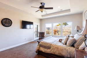 Bedroom with a raised ceiling, access to exterior, ceiling fan, and carpet