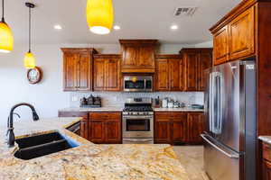 Kitchen featuring decorative backsplash, light stone countertops, stainless steel appliances, sink, and decorative light fixtures