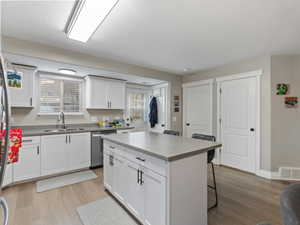 Kitchen with sink, dishwasher, a center island, white cabinetry, and a breakfast bar area