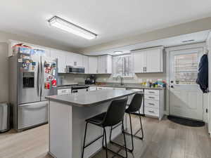 Kitchen with white cabinetry, a center island, sink, stainless steel appliances, and a kitchen breakfast bar