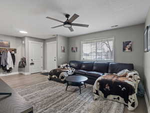 Living room with ceiling fan, light wood-type flooring, and a textured ceiling