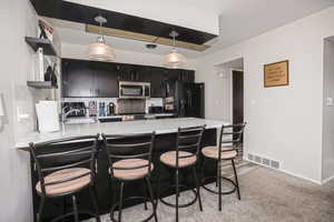 Kitchen featuring black refrigerator with ice dispenser, hanging light fixtures, sink, a kitchen bar, and kitchen peninsula