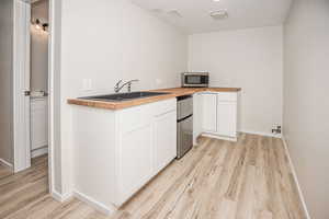 Kitchen featuring sink, butcher block countertops, light hardwood / wood-style floors, fridge, and white cabinets