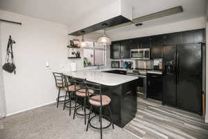 Kitchen featuring kitchen peninsula, tasteful backsplash, a breakfast bar, stainless steel appliances, and hanging light fixtures