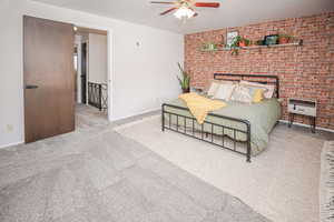 Carpeted bedroom with ceiling fan and brick wall