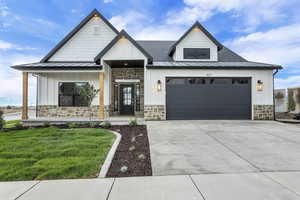 Modern farmhouse with a garage, concrete driveway, stone siding, a standing seam roof, and a front lawn