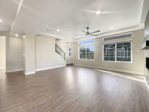 Unfurnished living room featuring a tray ceiling, ceiling fan, and hardwood / wood-style floors