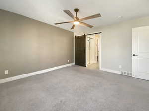 Unfurnished bedroom with a barn door, ceiling fan, and light colored carpet