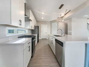 Kitchen featuring appliances with stainless steel finishes, sink, decorative light fixtures, light hardwood / wood-style flooring, and white cabinets