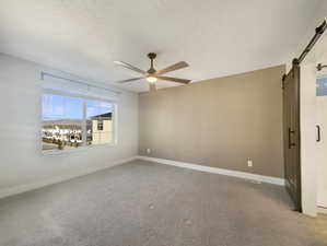 Unfurnished room featuring a barn door, ceiling fan, carpet floors, and a textured ceiling