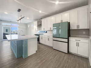 Kitchen with appliances with stainless steel finishes, sink, wall chimney range hood, decorative light fixtures, and white cabinetry