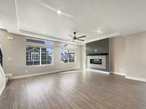 Unfurnished living room with hardwood / wood-style flooring, a raised ceiling, and ceiling fan