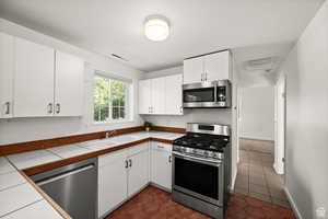 ADU - Kitchen featuring white cabinetry, sink, stainless steel appliances, dark tile patterned floors, and tile countertops