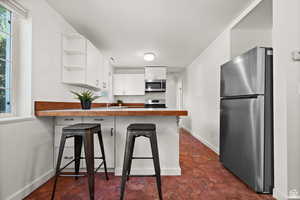 ADU - Kitchen featuring white cabinetry, dark tile patterned floors, kitchen peninsula, a breakfast bar, and appliances with stainless steel finishes