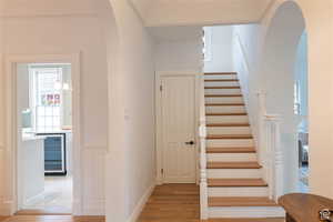 Staircase with wood-type flooring, ornamental molding, and beverage cooler