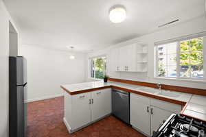 ADU - Kitchen with tile countertops, white cabinets, sink, appliances with stainless steel finishes, and kitchen peninsula, lots of room for a table as well.