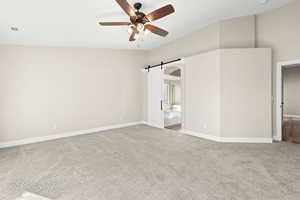 Spare room featuring ceiling fan, a barn door, and light colored carpet