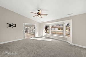 Unfurnished living room featuring a textured ceiling, carpet floors, vaulted ceiling, and ceiling fan