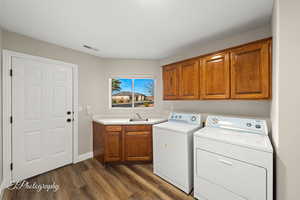 Laundry room with washer and clothes dryer, cabinets, sink, and dark wood-type flooring