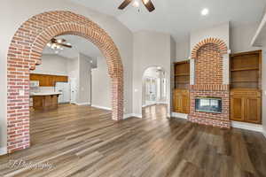 Unfurnished living room with ceiling fan, dark hardwood / wood-style floors, high vaulted ceiling, and a brick fireplace