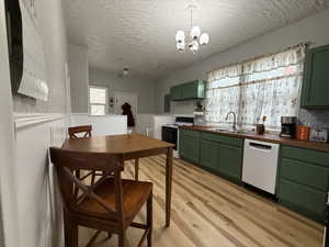 Kitchen featuring green cabinetry, white appliances, sink, and wooden counters