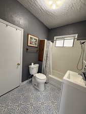 Full bathroom featuring sink, shower / tub combo with curtain, a textured ceiling, and toilet