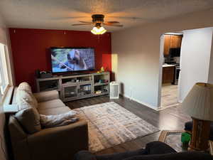 Living room featuring ceiling fan, dark wood-type flooring, and a textured ceiling