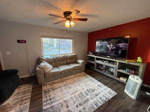 Living room with a textured ceiling, dark hardwood / wood-style flooring, and ceiling fan