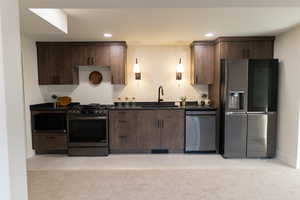 Kitchen featuring dark brown cabinets, sink, light colored carpet, and stainless steel appliances