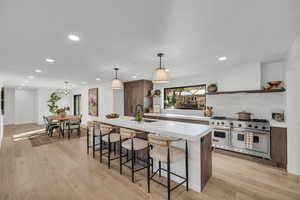 Kitchen with decorative light fixtures, sink, range with two ovens, an island with sink, and light hardwood / wood-style floors