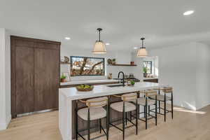 Kitchen featuring sink, light hardwood / wood-style floors, a kitchen island with sink, and pendant lighting