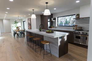 Kitchen featuring tasteful backsplash, pendant lighting, designer range, dark brown cabinets, and a center island with sink