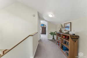 Hallway with a textured ceiling, light colored carpet, and lofted ceiling