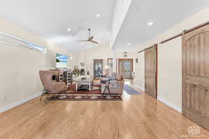 Living room with ceiling fan, a barn door, vaulted ceiling, and light hardwood / wood-style flooring