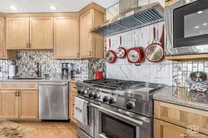 Kitchen featuring decorative backsplash, appliances with stainless steel finishes, light stone countertops, wall chimney exhaust hood, and light hardwood / wood-style floors