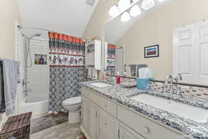 Full bathroom featuring hardwood / wood-style floors, vanity, lofted ceiling, toilet, and shower / bathtub combination with curtain