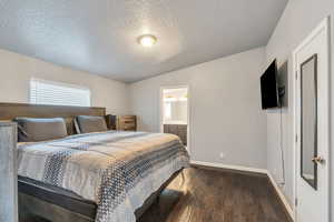 Bedroom with dark hardwood / wood-style flooring, lofted ceiling, a textured ceiling, and ensuite bath