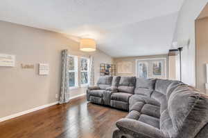 Living room with a textured ceiling, dark hardwood / wood-style flooring, and vaulted ceiling