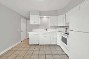 Kitchen featuring white cabinets, white appliances, light tile patterned flooring, and sink