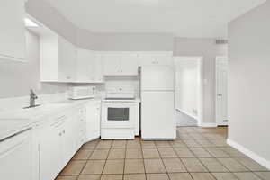 Kitchen with white cabinets, light tile patterned floors, white appliances, and sink