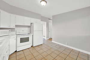 Kitchen with tile countertops, white cabinets, white appliances, and light tile patterned floors