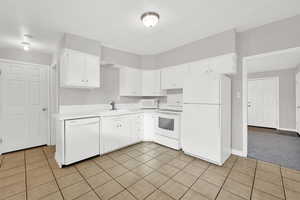 Kitchen featuring white cabinets, light tile patterned floors, white appliances, and sink