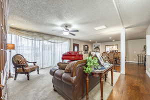 Living room with ceiling fan, a textured ceiling, and hardwood / wood-style flooring