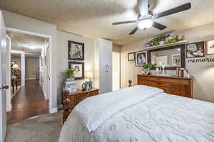 Carpeted bedroom with ceiling fan and a textured ceiling