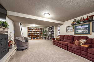 Living room with carpet flooring, a textured ceiling, and a stone fireplace