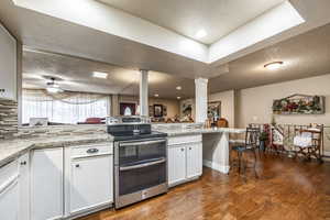 Kitchen featuring a kitchen bar, kitchen peninsula, ceiling fan, white cabinetry, and stainless steel range with electric cooktop